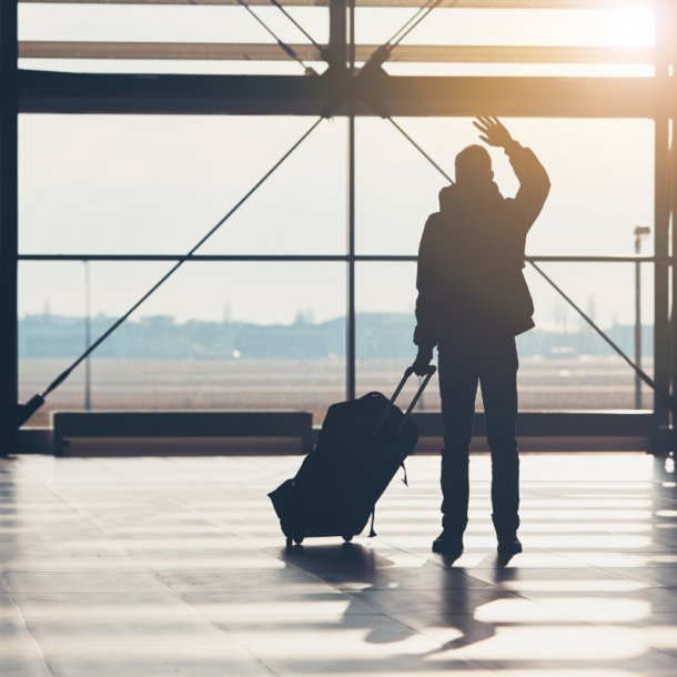 Silhouetted person at the airport with luggage waving goodbye