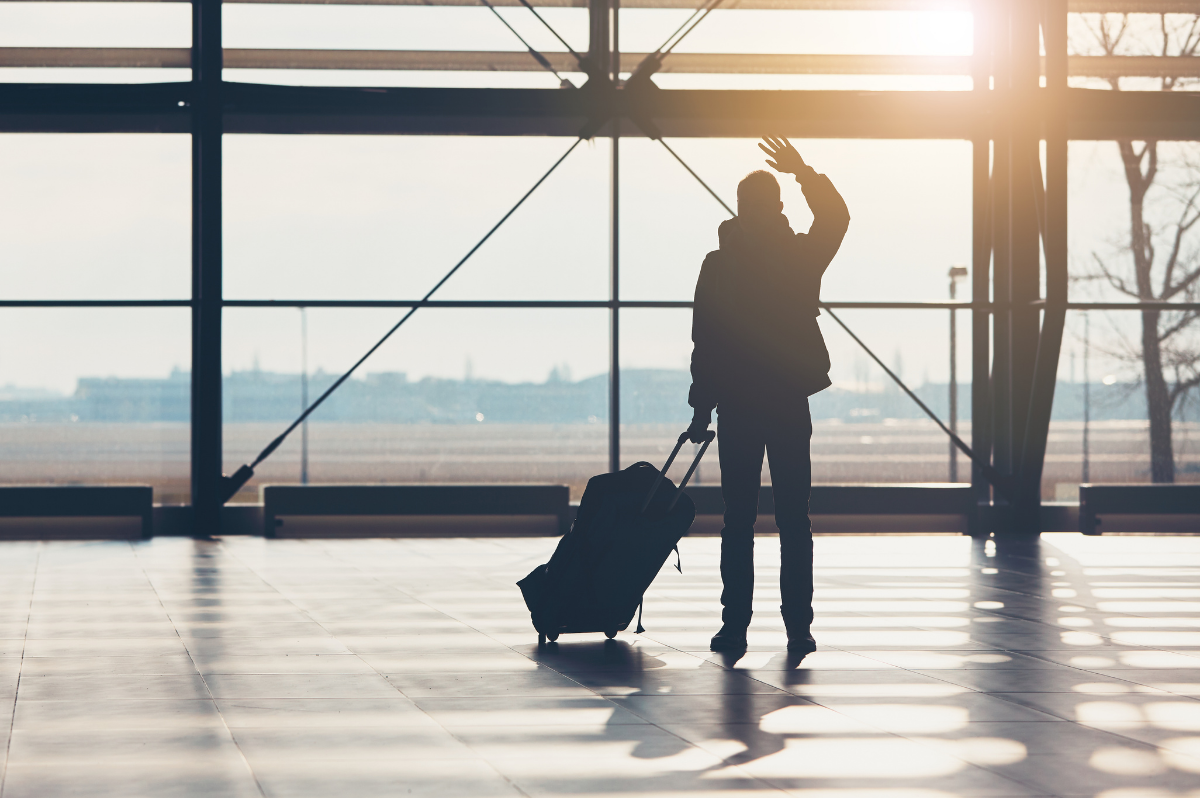 Silhouetted person at the airport with luggage waving goodbye