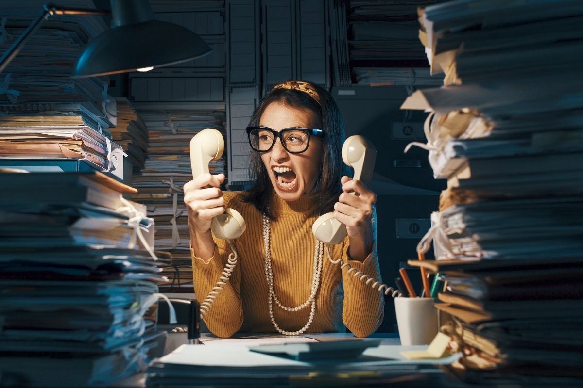 woman between stacks of paper, screaming with an old telephone in each hand