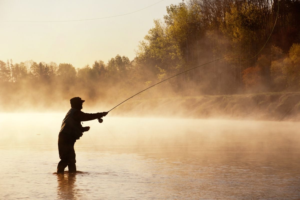 silhouette of a man fly fishing in the middle of a river