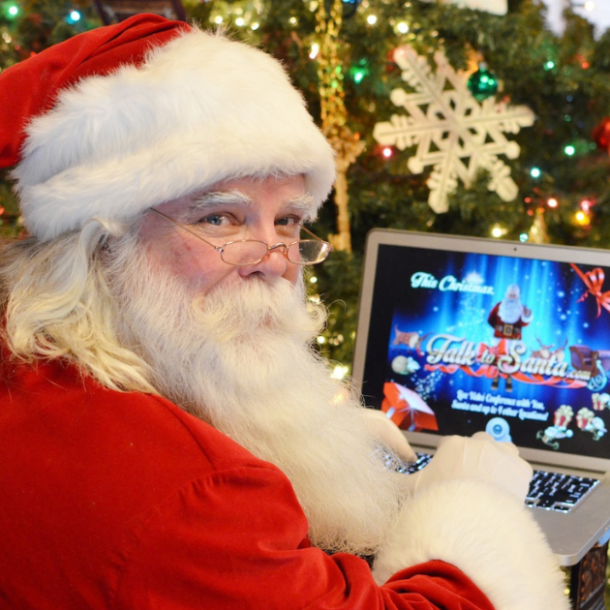 Santa Claus looking back over his shoulder holding a laptop with the Talk to Santa website on it