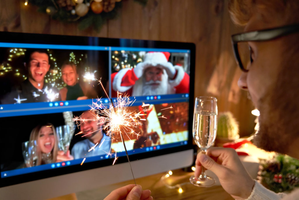 Young man wears Christmas hat drinking champagne holding sparkler talking to friends on virtual video call celebrate Happy New Year party in distance online chat at home, over shoulder screen view.